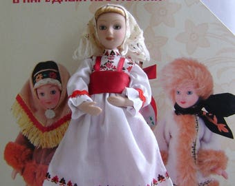 May include: Three dolls wearing traditional Russian folk costumes. The doll in the center is wearing a white dress with red and black embroidery, a red sash, and a white head scarf. The doll on the left is wearing a brown and white costume with a white head scarf. The doll on the right is wearing a brown and white costume with a brown fur trim and a black head scarf. The dolls are standing on a white background. The text on the book behind the dolls reads "Куклы в народных костюмах".