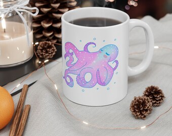 May include: White ceramic mug with a pink and blue galaxy octopus illustration. The octopus has a sleepy expression and is surrounded by small white circles.