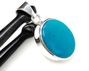 Puede incluir: Un colgante de plata con una gran piedra ovalada de turquesa. La piedra es de un color azul vibrante y tiene un acabado liso y pulido.