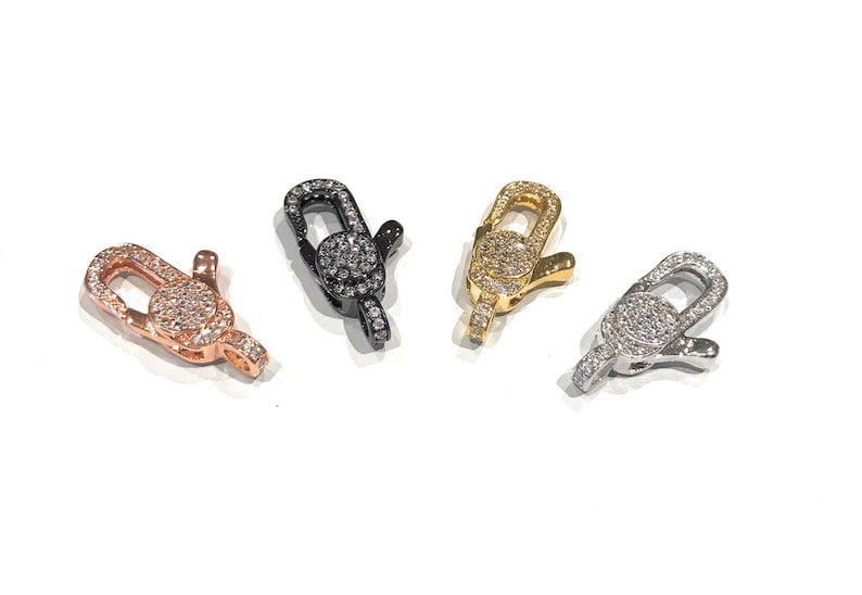 K&ouml;nnte beinhalten: Vier Hummerklauenverschl&uuml;sse mit klaren Strasssteinen. Die Verschl&uuml;sse sind in vier verschiedenen Ausf&uuml;hrungen erh&auml;ltlich: Ros&eacute;gold, Schwarz, Gold und Silber.