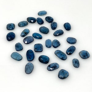 May include: A collection of 20 blue kyanite gemstone cabochons, each with a unique shape and size. The stones have a deep blue color with a slight shimmer.