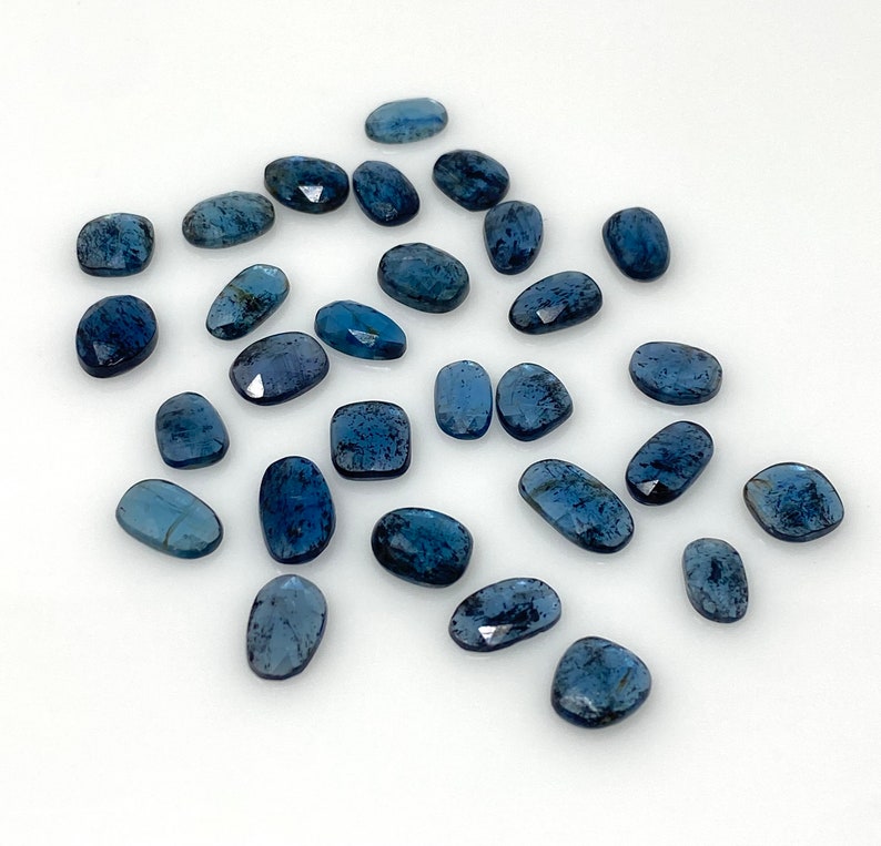 May include: A collection of 20 blue kyanite gemstone cabochons, each with a unique shape and size. The stones have a deep blue color with a slight shimmer.