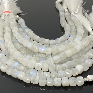 May include: A strand of white moonstone beads, each bead is faceted and has a square shape. The beads are strung on a silver thread and have a white tassel at each end.