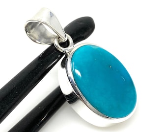 Puede incluir: Un colgante de plata con una gran piedra ovalada de turquesa. La piedra es de un color azul verdoso vibrante.