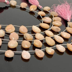 May include: A strand of pink opal gemstone beads, each bead is faceted and pear-shaped. The beads are strung on a silver wire and have pink tassels at the ends.