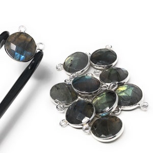 May include: A group of 10 silver-toned gemstone connector charms with a round, faceted labradorite stone. The stones are a dark green, blue, and black color with iridescent flashes.