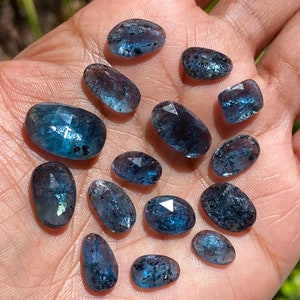 May include: A collection of 14 faceted aquamarine gemstones in various sizes and shapes. The stones are a light blue color with a slight shimmer.