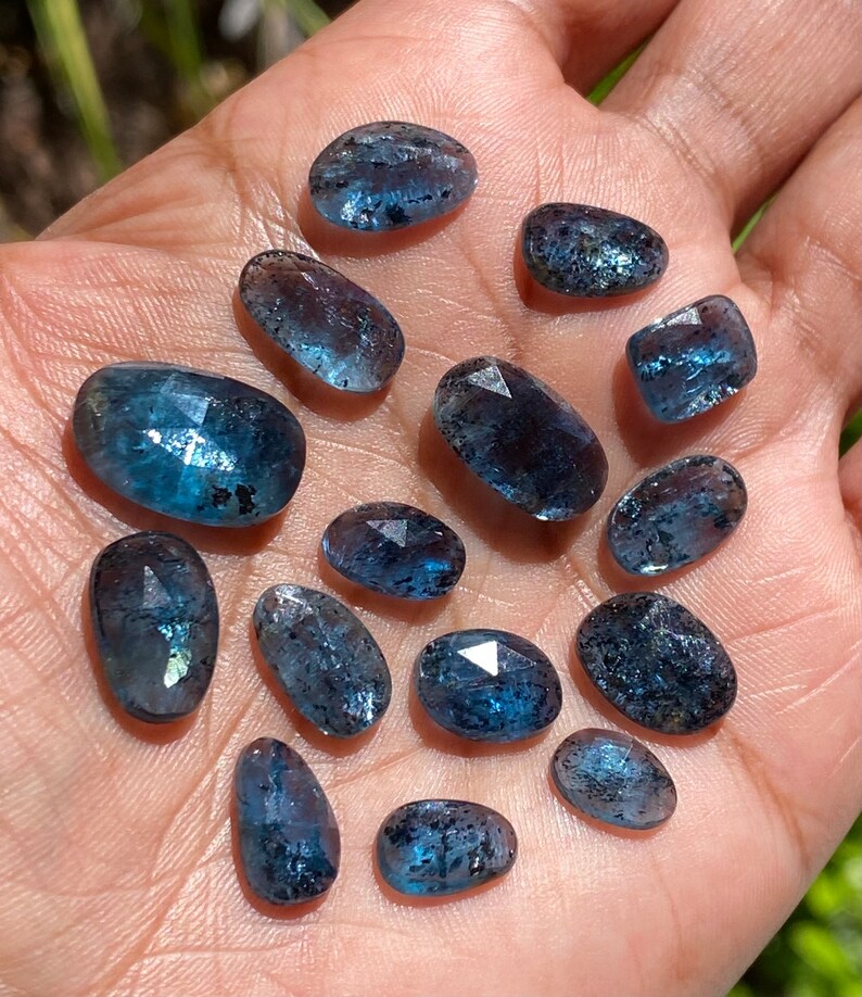 May include: A collection of 14 faceted aquamarine gemstones in various sizes and shapes. The stones are a light blue color with a slight shimmer.