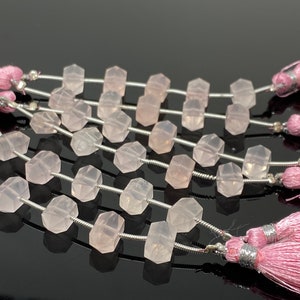 May include: Strands of faceted, light pink rose quartz beads. Each bead is strung on a silver-colored wire, with pink tassels at the ends. The beads have a geometric shape and a translucent quality.