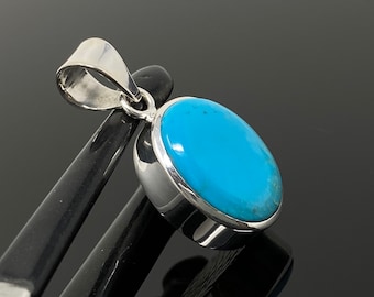 Puede incluir: Un colgante de plata con una piedra turquesa ovalada de color azul brillante.