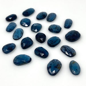 May include: A collection of 17 blue kyanite gemstone cabochons, each with a unique, faceted oval shape. The stones have a deep blue color with a slight shimmer.