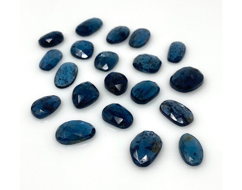 May include: A collection of 17 blue kyanite gemstone cabochons, each with a unique, faceted oval shape. The stones have a deep blue color with a slight shimmer.
