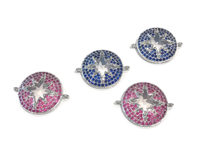 Pu&ograve; includere: Tre ciondoli a forma di stella argentati con centri in cristallo trasparente. I ciondoli sono circondati da strass blu e rosa.