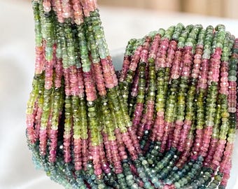 May include: A collection of faceted rondelle beads strung on multiple strands, featuring a gradient of colors including shades of pink, light green, olive green, and deep teal. The small, circular beads have a reflective, polished surface texture.