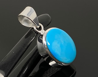 Puede incluir: Un colgante de plata con una piedra ovalada turquesa azul claro.