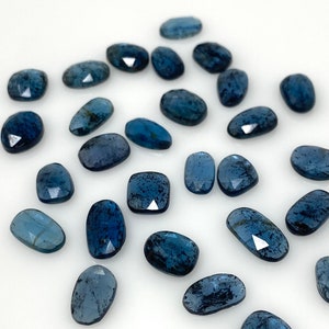 May include: A collection of 20 loose, faceted, blue-grey gemstone cabochons. The stones are oval shaped and have a speckled, cloudy appearance.