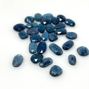 May include: A collection of 20 loose, faceted, oval-shaped blue kyanite gemstones. The stones are a deep blue color with a slight shimmer.