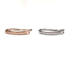May include: Two ear cuffs, one in rose gold and one in silver, with a row of small clear stones.
