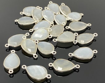 May include: A collection of teardrop-shaped, pale gray gemstone pendants with silver-colored metal edging and loops for attaching to jewelry. The pendants are faceted, catching the light and creating a subtle sparkle. The background is black.