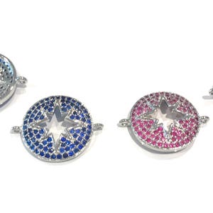 Pu&ograve; includere: Tre ciondoli rotondi argentati con un taglio a stella al centro. I ciondoli sono decorati con piccoli strass blu, rosa e trasparenti.