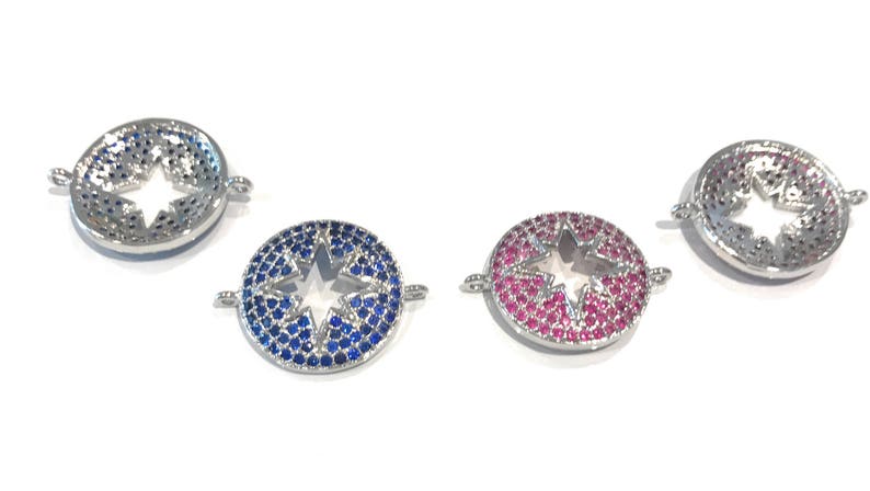 Pu&ograve; includere: Tre ciondoli rotondi argentati con un taglio a stella al centro. I ciondoli sono decorati con piccoli strass blu, rosa e trasparenti.