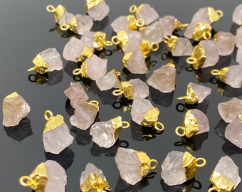 May include: A collection of pink quartz raw crystal charms with gold-plated jump rings. The charms are irregular in shape and have a natural, rough texture.
