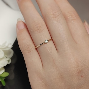 May include: A delicate gold ring with a single, small, clear gemstone set in the center.