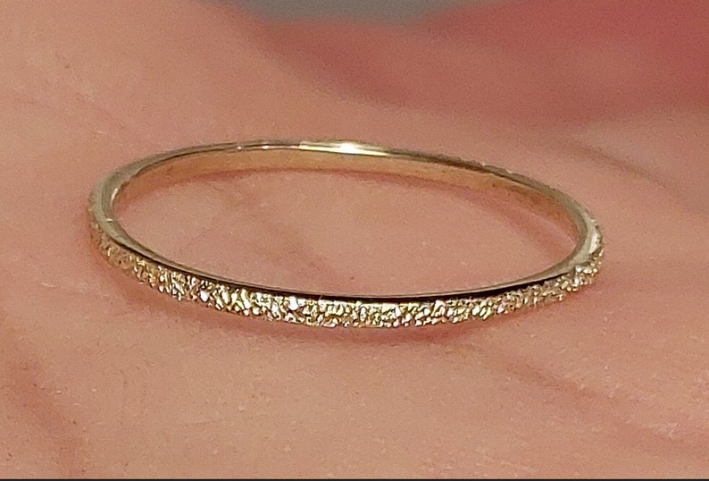 May include: A thin gold band ring with a textured surface.