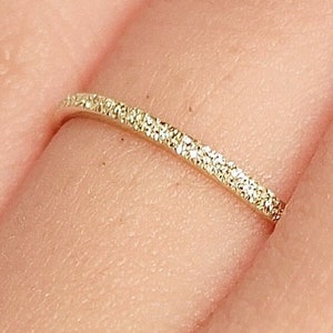 May include: A thin gold band ring with a sparkling diamond-like finish.