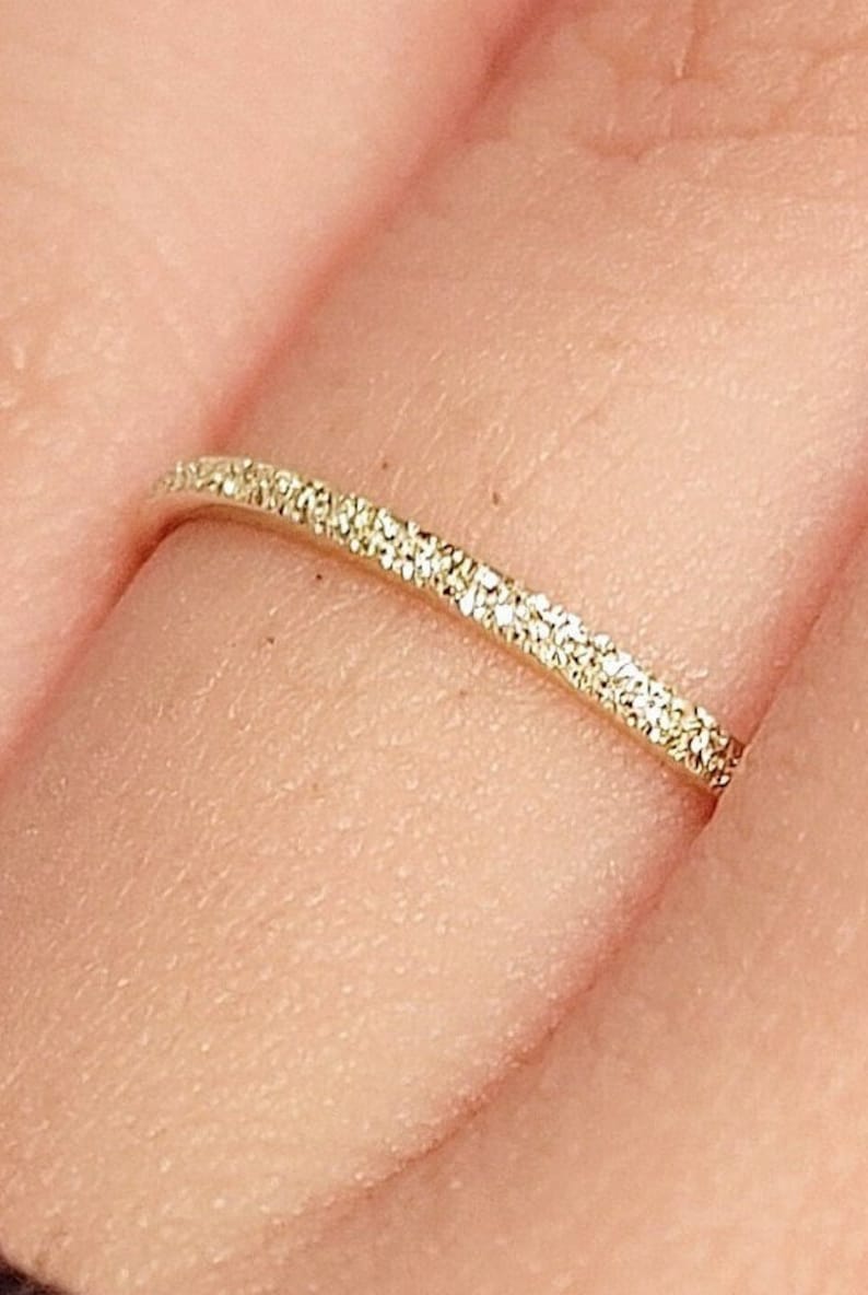 May include: A thin gold band ring with a sparkling diamond-like finish.