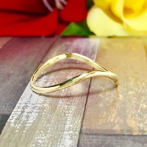 May include: A gold-colored ring with a unique, flowing design. The ring has a smooth, polished surface and a subtle wave shape. The ring is a piece of jewelry.