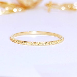 May include: A thin gold band ring with a textured surface.