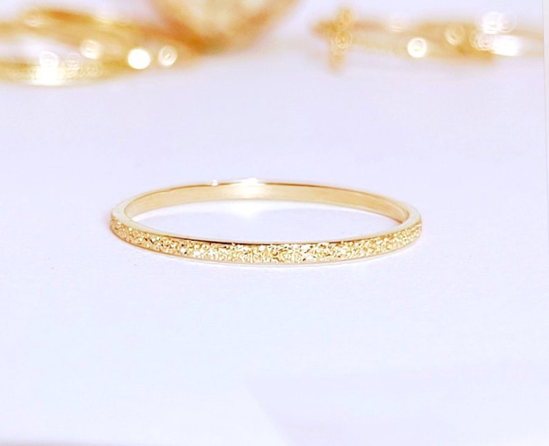 May include: A thin gold band ring with a textured surface.