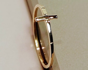 May include: A gold ring with a simple cross design. The ring is thin and delicate, and the cross is centered on the band.