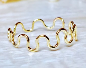 May include: A gold-colored ring with a wavy design. The ring is made of thin wire and has a delicate, feminine look.