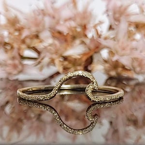 May include: A gold wave ring with a textured surface. The ring is delicate and has a simple design.