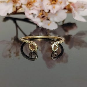 May include: A gold ring with a unique design featuring two open loops adorned with small sparkling stones.