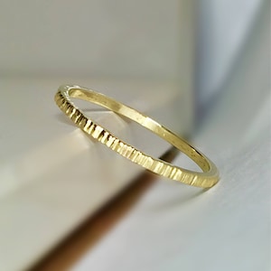 May include: A thin gold band ring with a textured, ridged design.