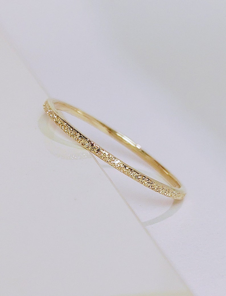 May include: A thin gold band ring with a textured surface.