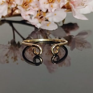 May include: A gold ring with two curved, open ends. The ring is on a black reflective surface.