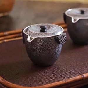 Może przedstawiać: Dwa srebrne czajniki z czarnymi drewnianymi uchwytami i pokrywkami na brązowej bambusowej tacy.