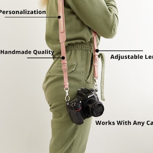 May include: A pink leather camera strap with adjustable length. The strap is worn by a person with a camera attached. The strap has the text "Free Personalization" and "100% Handmade Quality" printed on it. The text "Adjustable Length" and "Works With Any Camera" are also included in the image.