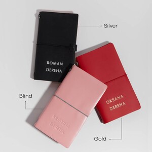 May include: Three leather journals in black, red, and pink. Each journal has a matching elastic band closure and personalized text. The black journal has silver text, the red journal has gold text, and the pink journal has blind debossed text.
