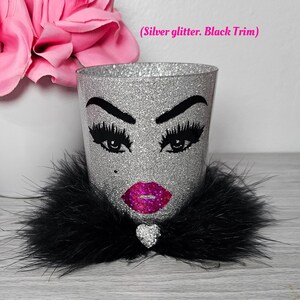 May include: Silver glitter makeup brush holder with a black faux fur trim, a black and white illustration of a face with eyelashes, lips, and a rhinestone heart.