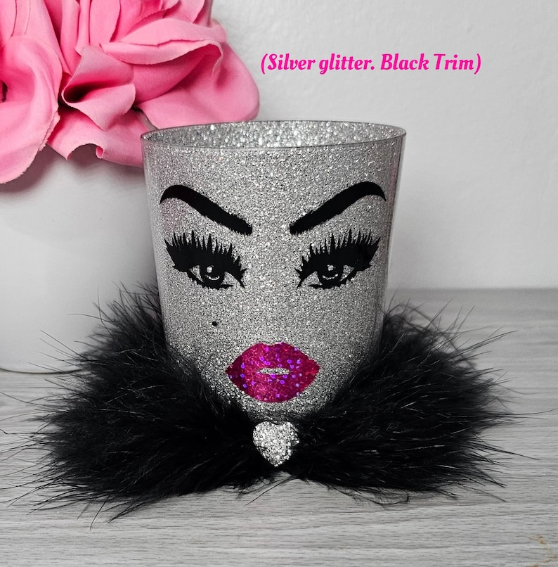 May include: Silver glitter makeup brush holder with a black faux fur trim, a black and white illustration of a face with eyelashes, lips, and a rhinestone heart.