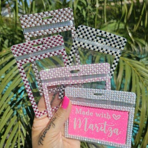 May include: Four clear plastic badge holders with different colored rhinestone borders. The holders are decorated with rhinestones and have a zipper closure. The bottom holder has a pink background with the text "Made with ♥ Maritza".