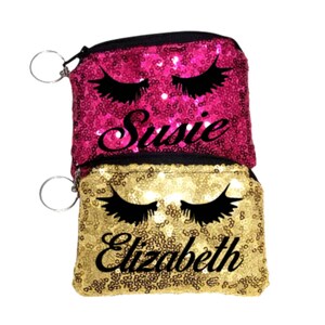 May include: Two gold and pink sequin coin purses with black eyelashes and personalized names. The pink purse says "Susie" and the gold purse says "Elizabeth".