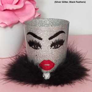May include: Silver glitter makeup brush holder with black feather trim and a black and white face with red lips design. (Silver Glitter. Black Feathers)