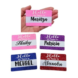 May include: A collection of glittery name tags in pink, purple, blue, and red. Each tag has the words "Hello My Name Is" above a white section with a name written in cursive. Names include Maritza, Hailey, Patricia, Michael, and Alexandra.