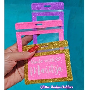 May include: Glitter badge holders in pink, gold, and purple. The gold holder has the text "Made with Maritza" in white. The holders have a clear plastic window and a slot for a lanyard. The text "Glitter Badge Holders" is at the bottom.
